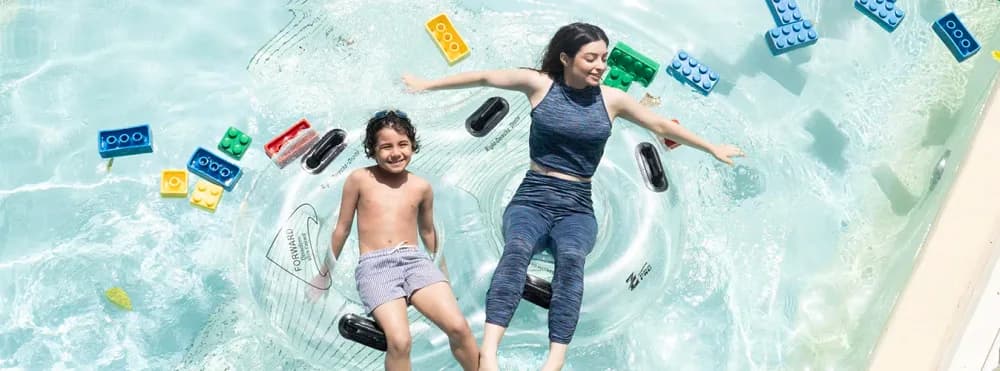 A parent and child floating together with LEGO bricks on Build-A-Raft River